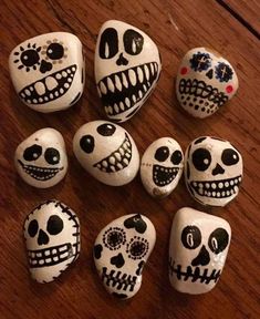 several skulls painted on rocks sitting on a wooden table next to a cell phone and pen