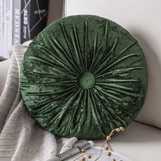 a green round pillow sitting on top of a white couch next to a book shelf