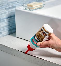 a hand holding a bottle of glue over a sink