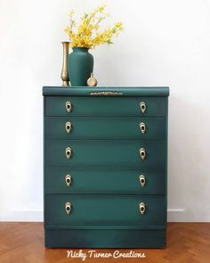 a green chest of drawers with gold handles and knobs on the bottom, in front of a white wall