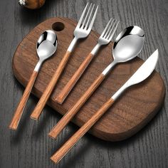 five spoons, two forks and one knife on a cutting board with wood handles