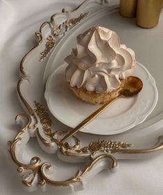 a white plate topped with a pastry covered in whipped cream next to a gold spoon