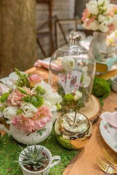 a wooden table topped with plates and vases filled with flowers next to a glass cloche dome