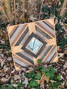 a mirror sitting on top of leaves in front of a wooden frame with a tree