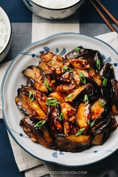 a white plate topped with fried eggplant next to rice and chopsticks