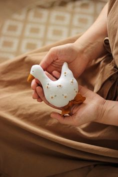 a person holding a white bird shaped object in their left hand and brown pants on the floor