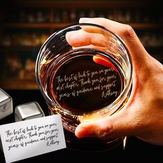 a person holding a glass with some kind of writing on it next to an ice cube