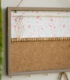 a cork bulletin board hanging on a wall next to a potted plant and beaded necklace