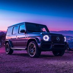 the mercedes benz g - class is parked on top of a hill at night with mountains in the background