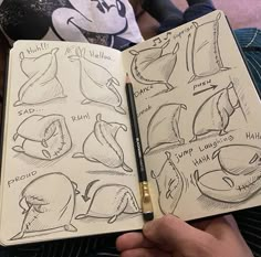 a hand holding an open notebook with sketches of mickey mouse's faces on it