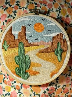 a hand embroidered desert scene with cactus trees and mountains in the background, on a floral fabric