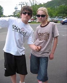 two young people standing next to each other in a parking lot with their arms outstretched