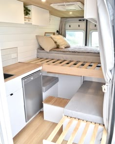 the interior of a camper with wood flooring and white walls, built in to an open kitchen area