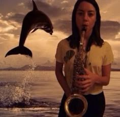 a woman is playing the saxophone while a dolphin jumps out of the water behind her