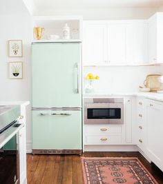 a green refrigerator in a white kitchen next to a rug and stove with gold accents