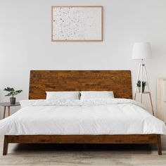 a bed with white sheets and pillows in a room next to a lamp on a table