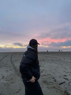 a woman standing on top of a sandy beach next to the ocean under a cloudy sky