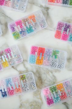 several plastic containers filled with colorful beads on top of a marble countertop next to each other