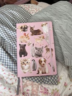 a pink notebook with pictures of dogs and cats on it sitting on top of a bed