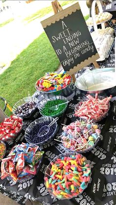 a table full of candy and candies for sale at an outdoor event with a chalkboard sign