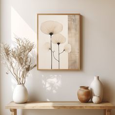 three white vases are sitting on a wooden table in front of a framed art piece