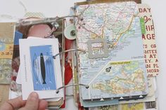 a person holding up a small book with maps on it and a pen sticking out of the cover