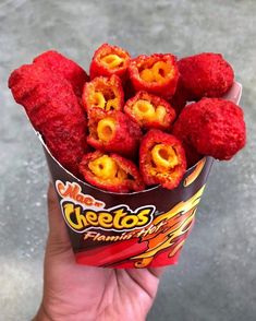 a hand holding up a cup filled with red candy covered in yellow and orange flakes