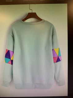 a sweater hanging on a hanger in front of a white wall with a colorful geometric design