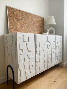 a white cabinet sitting on top of a hard wood floor next to a wall mounted lamp