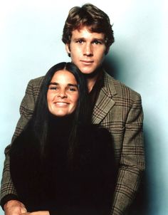 a man and woman posing for a photo in front of a blue wall with their arms around each other