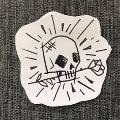 a sticker with a skull on it sitting on a piece of paper in front of a gray background