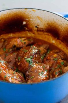 a blue pot filled with meat covered in gravy and garnished with parsley