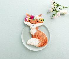 an embroidered fox brooch sits on a plate next to flowers