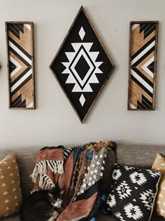 a living room filled with lots of pillows on top of a couch next to two wall hangings