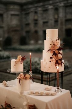 three tiered white wedding cake with flowers and candles sitting on top of a table