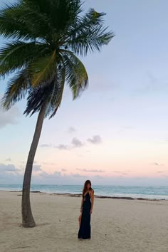 a woman standing on top of a sandy beach next to a palm tree in front of the ocean