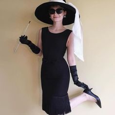 a woman in a black dress and hat holding a stick