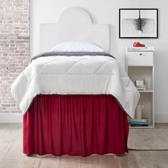 a bed with a white headboard and red bedspread next to a brick wall