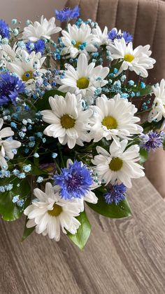 a bouquet of white and blue flowers sitting on top of a wooden table next to a chair