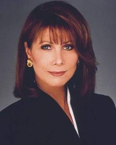 a woman with brown hair and blue eyes wearing a black blazer over a white shirt