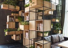 a room filled with lots of plants and bookshelves next to a couch in front of a window