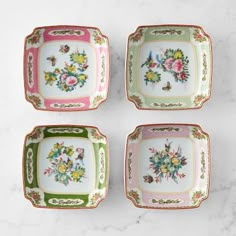 four plates with flowers painted on them sitting on a marble counter top, one is green and the other is pink