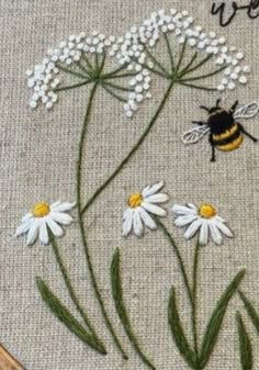 a close up of a cross stitch with flowers and a bee on it