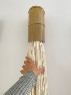 a hand reaching for a rope that is attached to a wall with a wooden pole