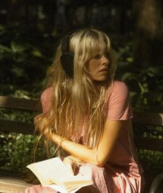 a woman sitting on a park bench with headphones in her ears reading a book