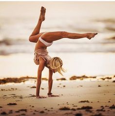 a woman doing a handstand on the beach with her feet in the air