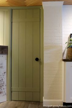 a green door in the corner of a room with white brick walls and wood flooring