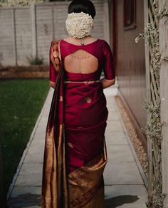 a woman in a red and gold sari walking down a sidewalk with her back to the camera