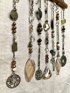 several different necklaces hanging from a wooden branch on a white cloth background with beads and charms attached to them