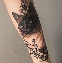 a black cat with blue eyes and flowers on its arm is shown in this tattoo design